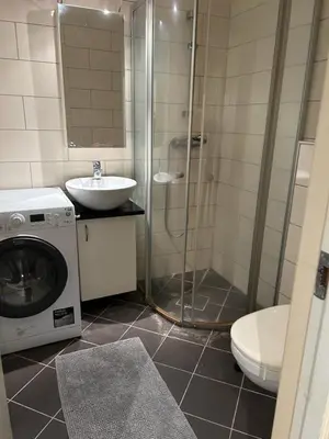 a bathroom with a shower and a sink and a washing machine at Marken Studio Apartments in Bergen