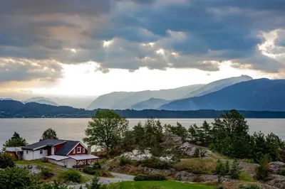 a house on a hill next to a body of water at Leilighet Vikaparken Hardangerfjord in Hatlestrand