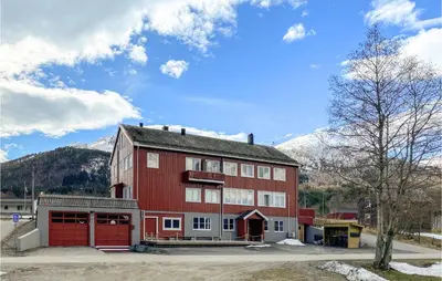 a large red building with mountains in the background at Pet Friendly Apartment In Tresfjord in Tresfjord