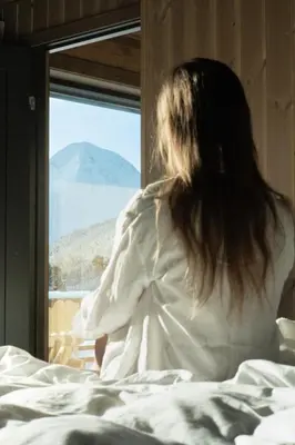 a woman sitting in bed looking out of a window at Dream Cabin Mivo X - Mountain Views and Idyllic Location at Strandafjellet in Stranda