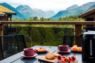 a table with plates of food on a balcony with mountains at 7 Min to Fjord - Alpine Stay in Stranda in Stranda