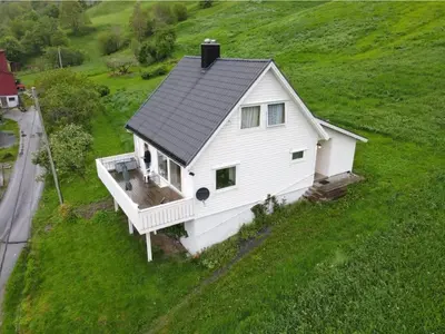 a white house on top of a green field at Enesi holiday house in Hestenesøyra