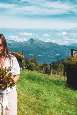 a woman standing in a field with a view of mountains at Exclusive Nordic Apartment with Sauna - Prime Location at Stranda near Geiranger in Stranda