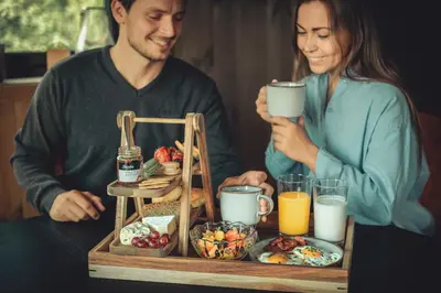 a man and woman sitting at a table with a tray of breakfast food at Nordic Luxury Apartment - Private Sauna & Panoramic Mountain Views in Stranda