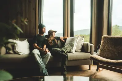 a man and woman sitting on a couch looking out a window at Nordic Luxury Apartment - Private Sauna & Panoramic Mountain Views in Stranda