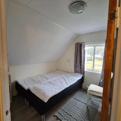 a small bed in a small room with a window at Koselig hus med hage i Herøy på Sunnmøre. in Røyra