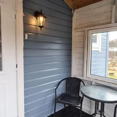 a table and chairs on a porch with a window at Koselig hus med hage i Herøy på Sunnmøre. in Røyra