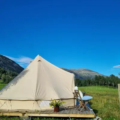 a canvas tent with a table and chairs in a field at Flatheim Glamping in Viksdalen