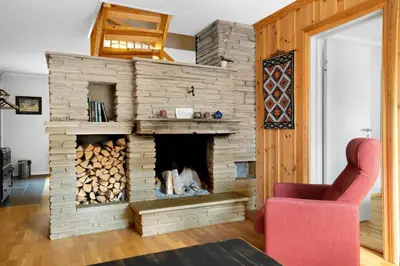 a living room with a stone fireplace with a red chair at Smuksjøseter Fjellstue in Høvringen
