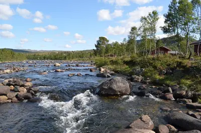 a river with rocks and a house in the background at Hovden Høyfjellsenter in Hovden