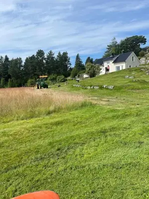 a field of green grass with a house and a tractor at Sjarmerende og romslig bolig, omgitt av vakker natur in Molde
