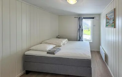 a small bedroom with a bed with white sheets and a window at Nice Home In Bremnes With Wifi in Bremnes