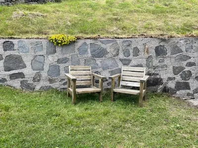 two wooden chairs sitting next to a stone wall at Feriehus i landlige område med nydelig utsikt in Leirvik