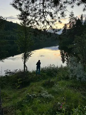 a person standing by a lake holding a fishing rod at Atnasjø Kafe AS in Sollia