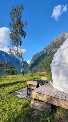 a tent and benches in a field with mountains at Olden Glamping - One with nature in Stryn