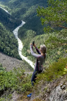 a woman standing on a hill taking a picture of a river at Groven Camping & Hyttegrend in Åmot