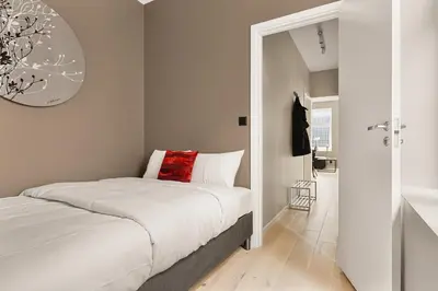 a white bedroom with a bed with a red pillow at Dinbnb Apartments I New 2023 I 600m to Bryggen in Bergen