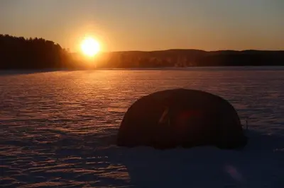 a tent on the water with the sunset in the background at Skomakerhuset in Løten