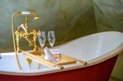 a bath tub with champagne glasses and a faucet at Charmante Skostredet Hôtel in Bergen