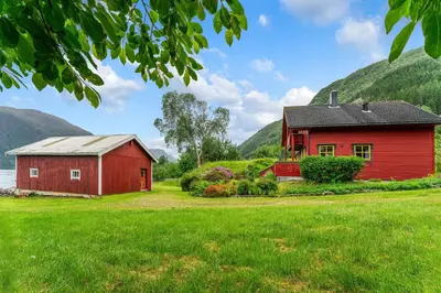 a red barn and a red house in a field at Fjord Lodge direkt am Ufer des Dalsfjord in Lauvstad