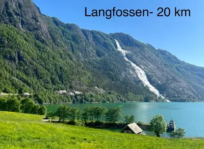 a mountain lake with a waterfall and a house in the foreground at Apartment-B near Etne-Odda in Etnesjøen