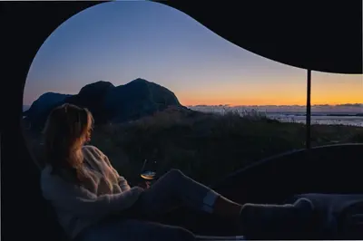 a woman sitting in a tent looking out at the sunset at Birdbox Reksta in Florø