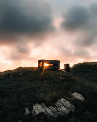 aburning bed on top of a grassy hill with the sunset at Birdbox Reksta in Florø