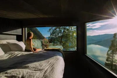 a woman sitting on a bed in a room with a large window at Sørheim FjordPanorama in Skjolden