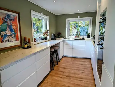 a kitchen with white cabinets and a wooden floor at Nyoppusset hus med utsikt. in Steinkjer