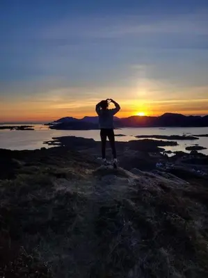 a person standing on the shore with the sunset in the background at Bellahuset - Charming House in Ulsteinvik in Ulsteinvik