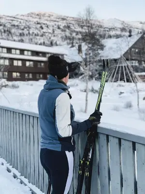 a woman is standing on a fence holding skis at Hovdestøylen Apartments in Hovden