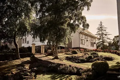 a white house with trees and flowers in front of it at Bekkjarvik Gjestgiveri in Bekkjarvik