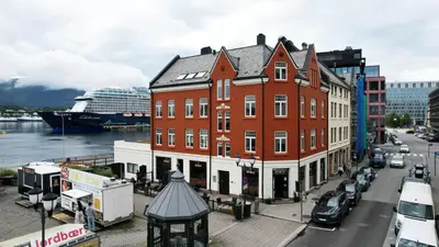 a large brick building on a city street with a cruise ship at West Coast Apartments Aalesund in Ålesund