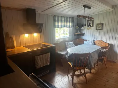 a living room with a table and a kitchen with a stove at Høstkos og ro på Budor, 4 roms hytte med peis og wifi in Nordset