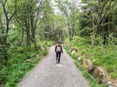 a woman walking down a path in the woods at Fresh studio apartment, a short walk from Bryggen in Bergen