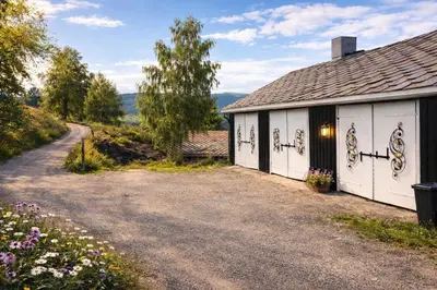 a house with a driveway next to a road at Sjarmerende tømmerhytte på gårdstun in Baukål