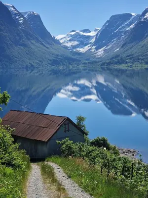 a barn on the side of a lake with snow covered mountains at Flo Bellevue in Stryn