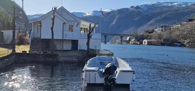 a boat parked in the water next to a house at Sjötun Fjord Cabin, with boat in Stanghelle