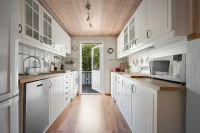 a kitchen with white cabinets and a wooden ceiling at Sjötun Fjord Cabin, with boat in Stanghelle
