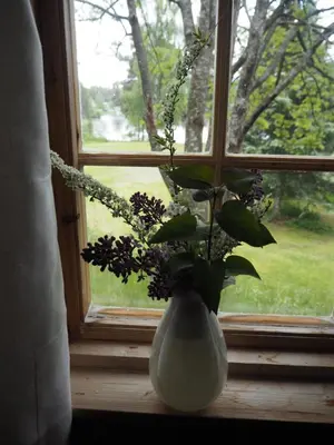 a white vase with flowers sitting on a window sill at Gamlestogo, Rønlund Hyttepark in Ron