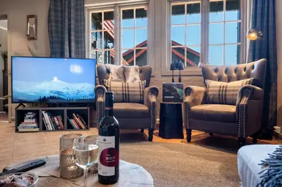 a living room with two chairs and a tv and a bottle of wine at Beitostølen! Midt i sentrum! Ski in ski out! Badstue-Massasjedusj-Steamdusj in Beitostøl