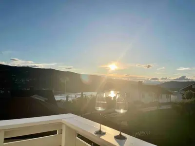 a view of the sunset from a balcony with two wine glasses at Solrikt og sentralt. Ta med både to og firbeinte in Lillehammer