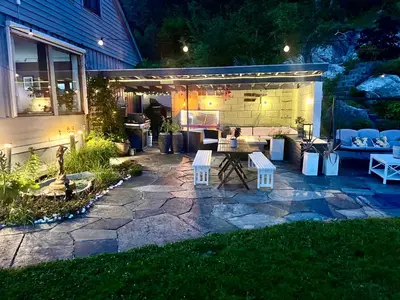a backyard patio at night with a table and chairs at Villa med panoramautsikt, stor uteplass og 100 m fra badestrand in Bergen