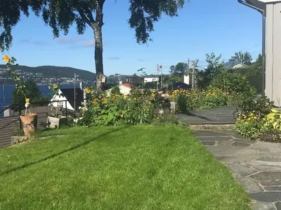a yard with green grass and flowers and a sidewalk at Villa med panoramautsikt, stor uteplass og 100 m fra badestrand in Bergen