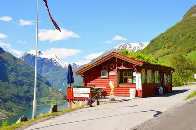 a small red cabin with mountains in the background at Hole Hytter in Geiranger