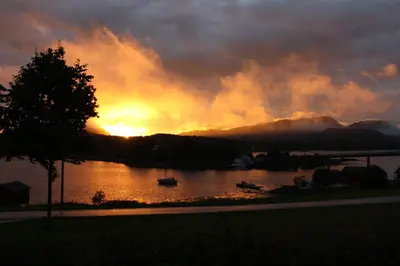 a sunset on a lake with a boat in the water at Åkviktunet hytte nord in Averoy