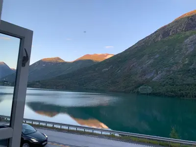 a car parked next to a lake with mountains at Stryn Golden Resort-«Skulehuset» in Stryn