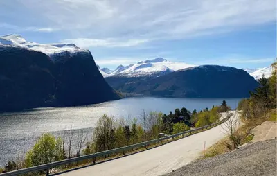 a road next to a lake with snow covered mountains at Lovely Home In Valldal in Valldal