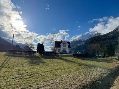 a house in a field with mountains in the background at Skogly - det gode livet på landet in Stryn