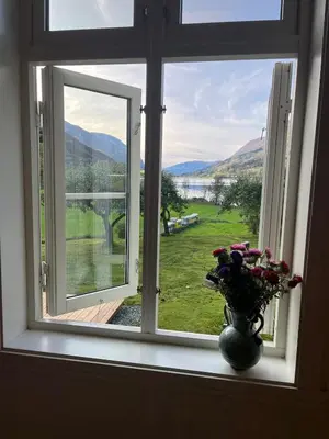 a window with a vase of flowers on a window sill at Skogly - det gode livet på landet in Stryn